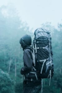 Man Wearing Black Hoodie Carries Black and Gray Backpacker Near Trees during Foggy Weather