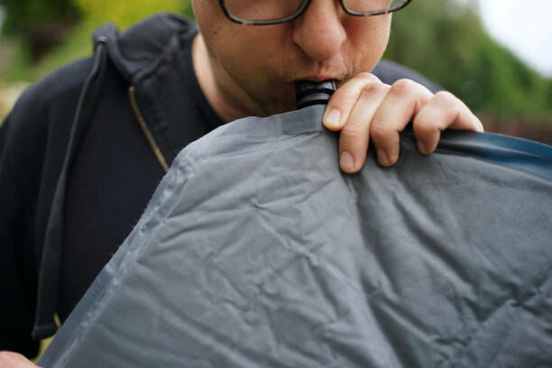 Close up of man with glasses blowing up a self inflatable sleeping pad for camping Close up of man with glasses blowing up a self inflatable sleeping pad for camping camping sleeping pad stock pictures, royalty-free photos & images